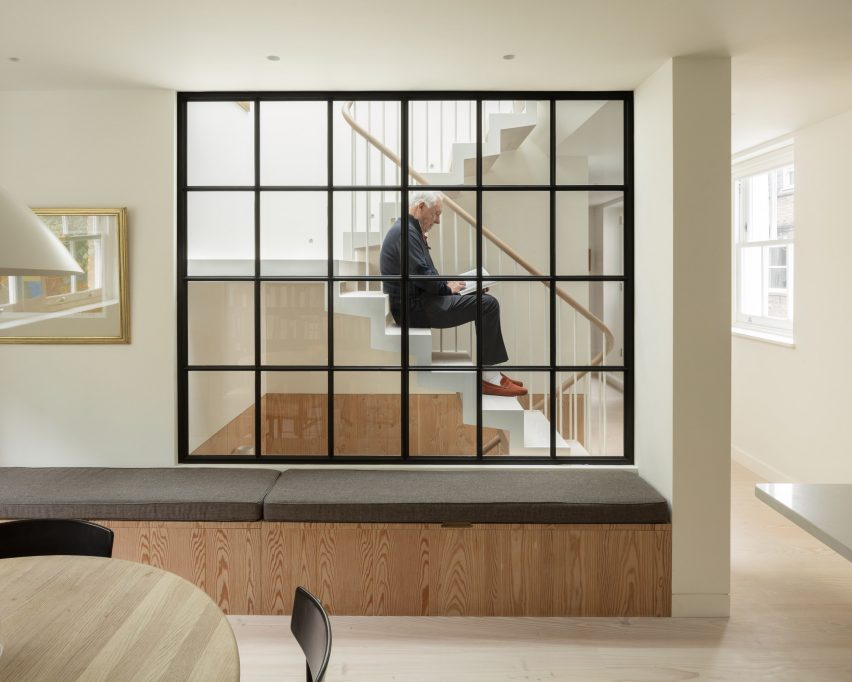 Man sitting on a staircase behind a wall of gridded glazing inside Danish Mews House by Neil Dusheiko Architects
