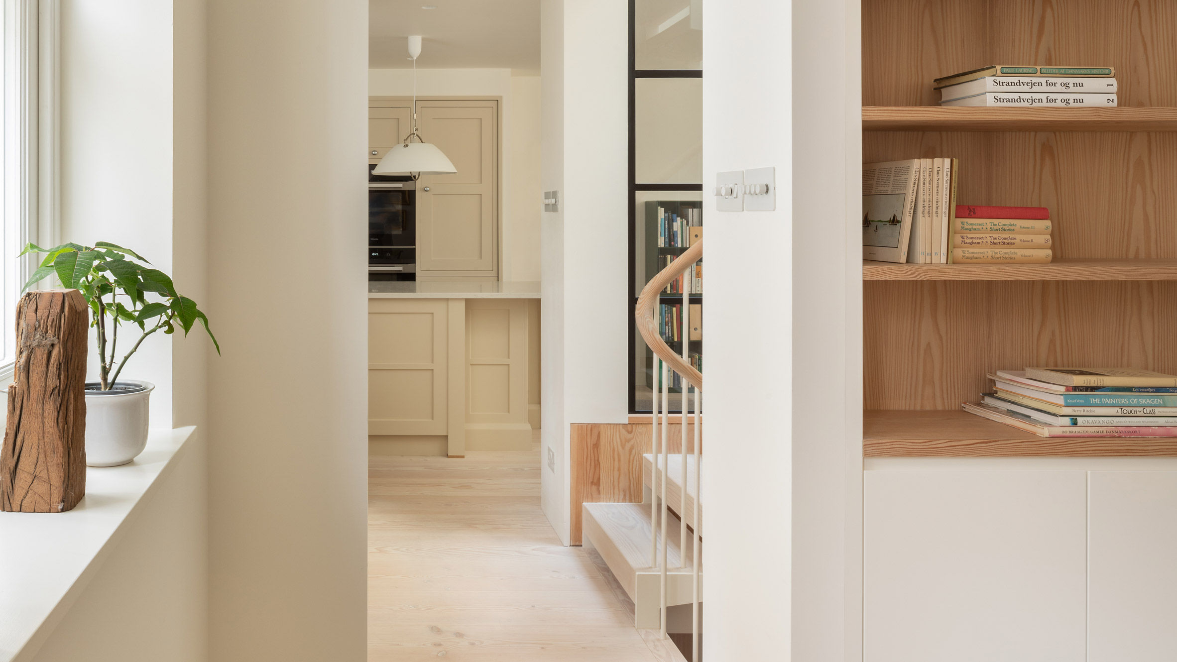 View of a bookshelf, staircase and kitchen on the interior of Danish Mews House by Neil Dusheiko Architects