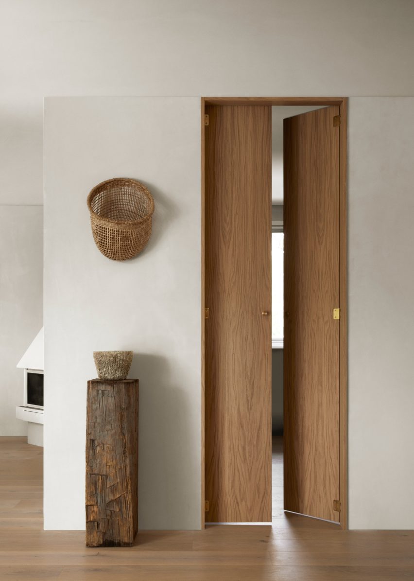 Full-height oak doors next to plinth holding ceramic vessel in forest retreat designed by Norm Architects