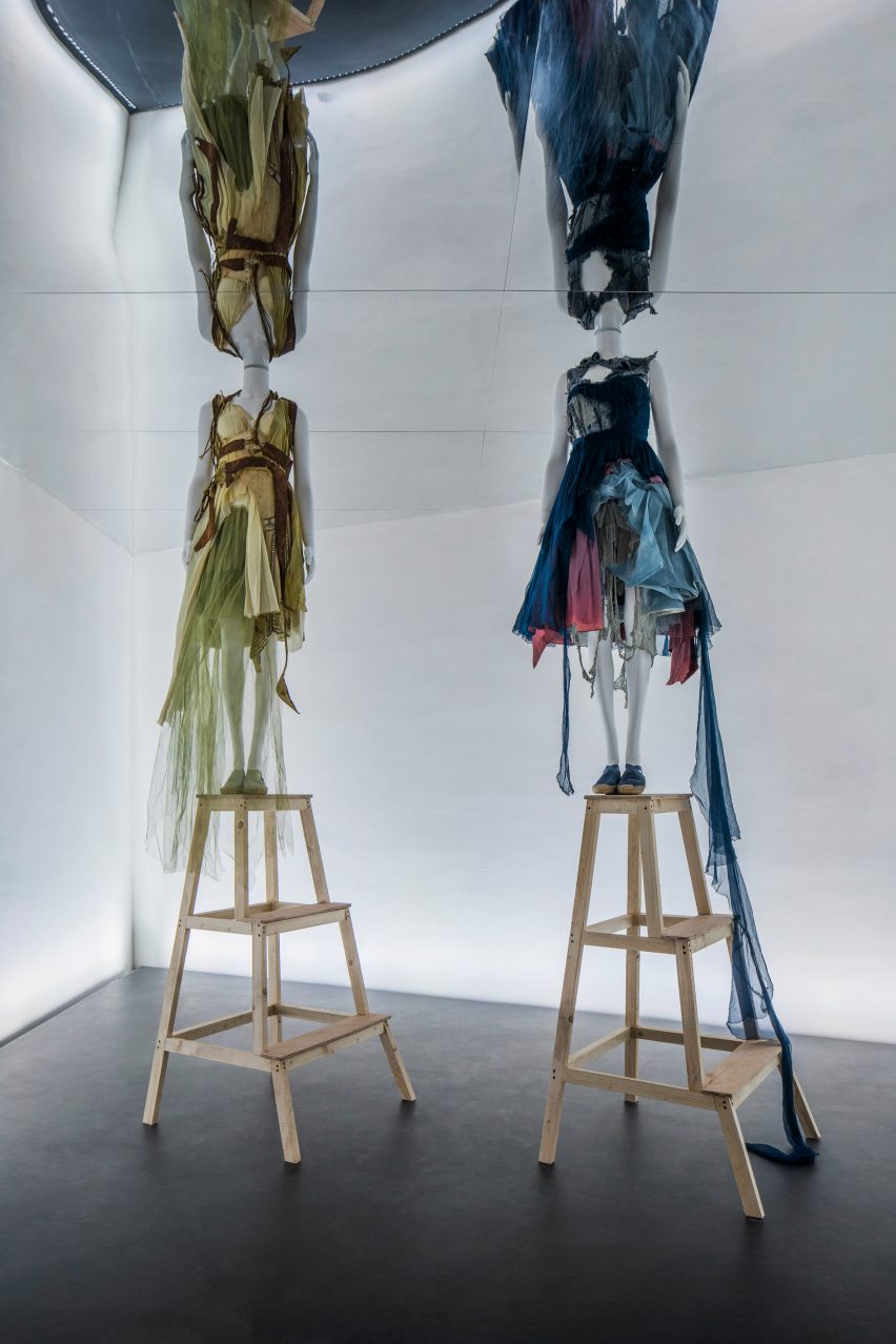 Mannequins dressed in Hussein Chalayan are positioned on step ladders below a mirrored ceiling