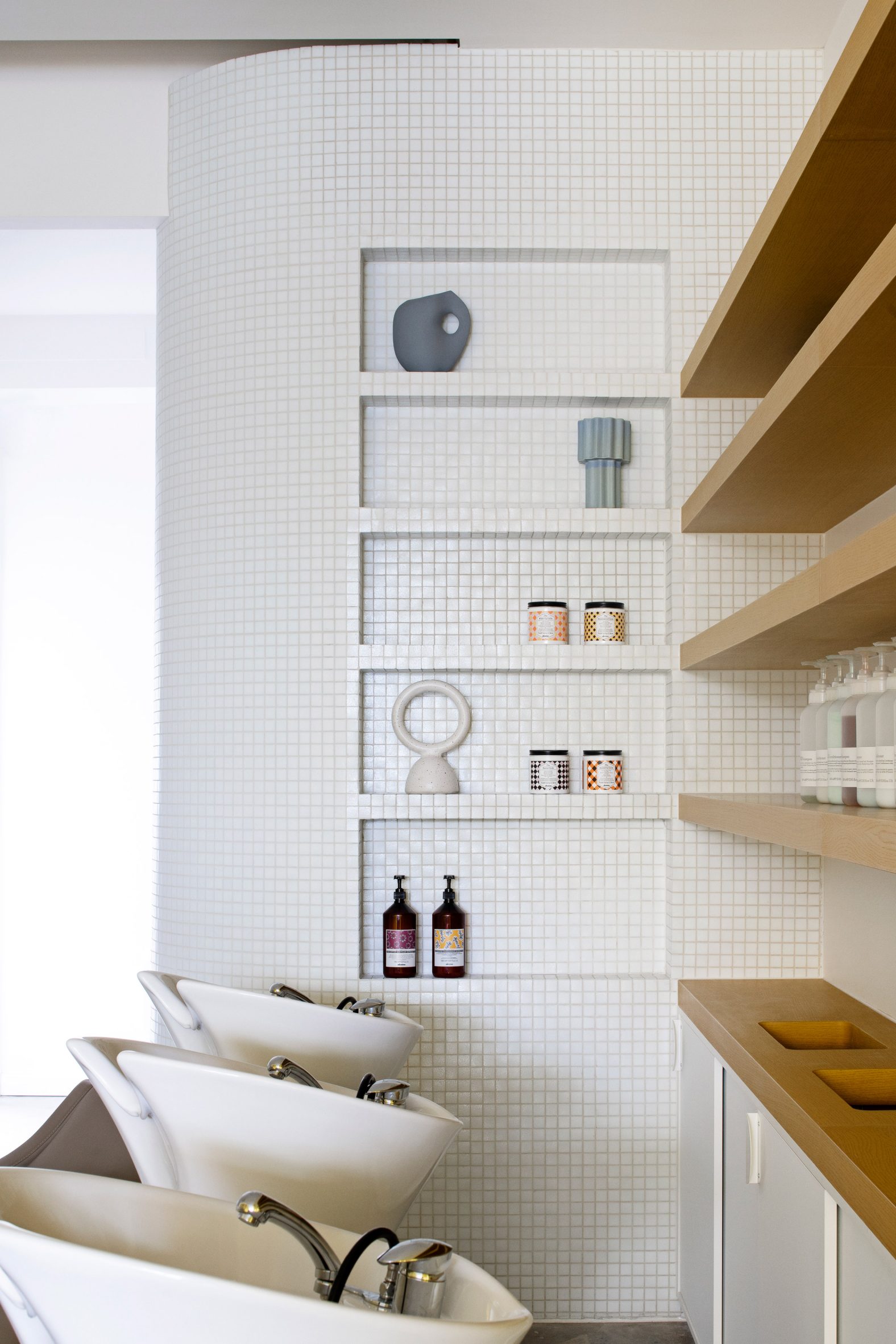 White-tiled built-in display shelf with decorative objects beside hair washing stations at Mitch Studio hairdressers