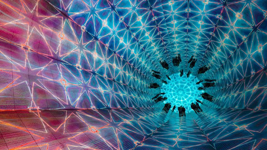 People walk through Stufish's giant kaleidoscope as it reflects a blue and purple digital pattern