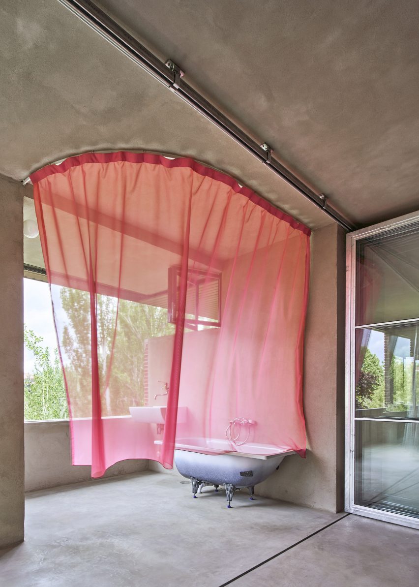 Bathtub on a balcony surrounded by a sheer pink curtain in apartment interior by Takk