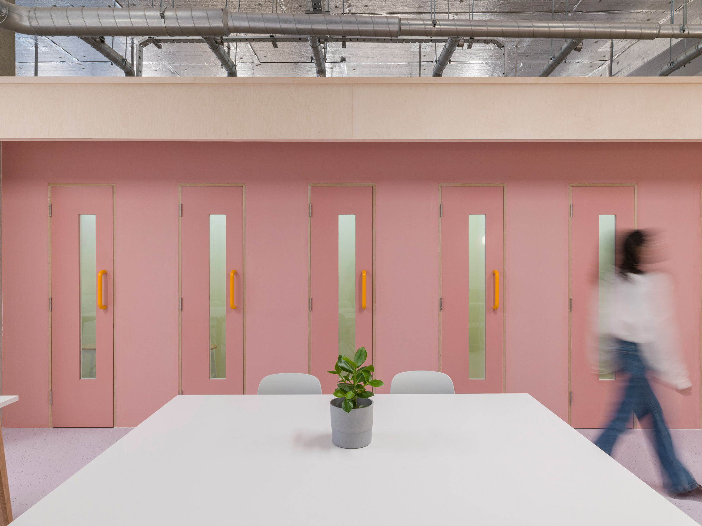 Row of phone booths with baby pink doors and orange handles in co-working office by Caro Lundin