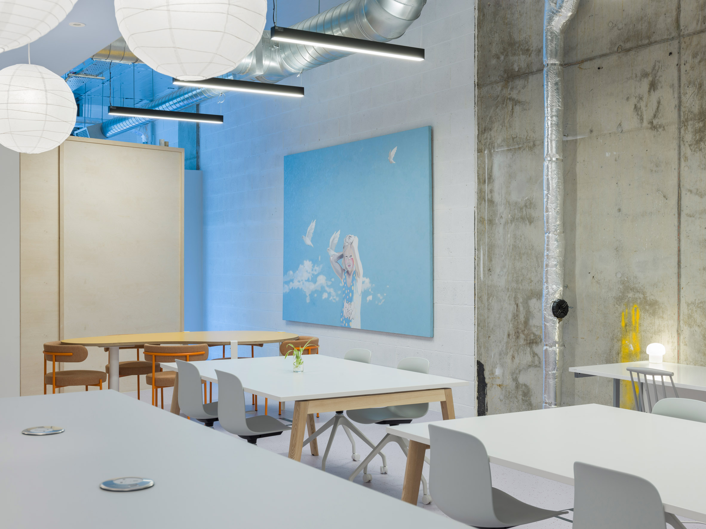 Interiors of co-working office by Caro Lundin with large tables surrounded by chairs in front of a blue artwork