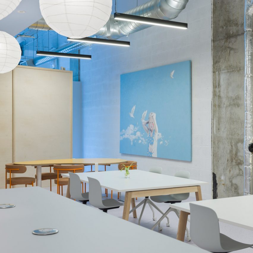 Interiors of ARC Club Camberwell co-working office by Caro Lundin with large tables surrounded by chairs in front of a blue artwork
