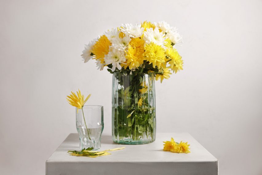 A clear glass and matching vase on a table with yellow flowers