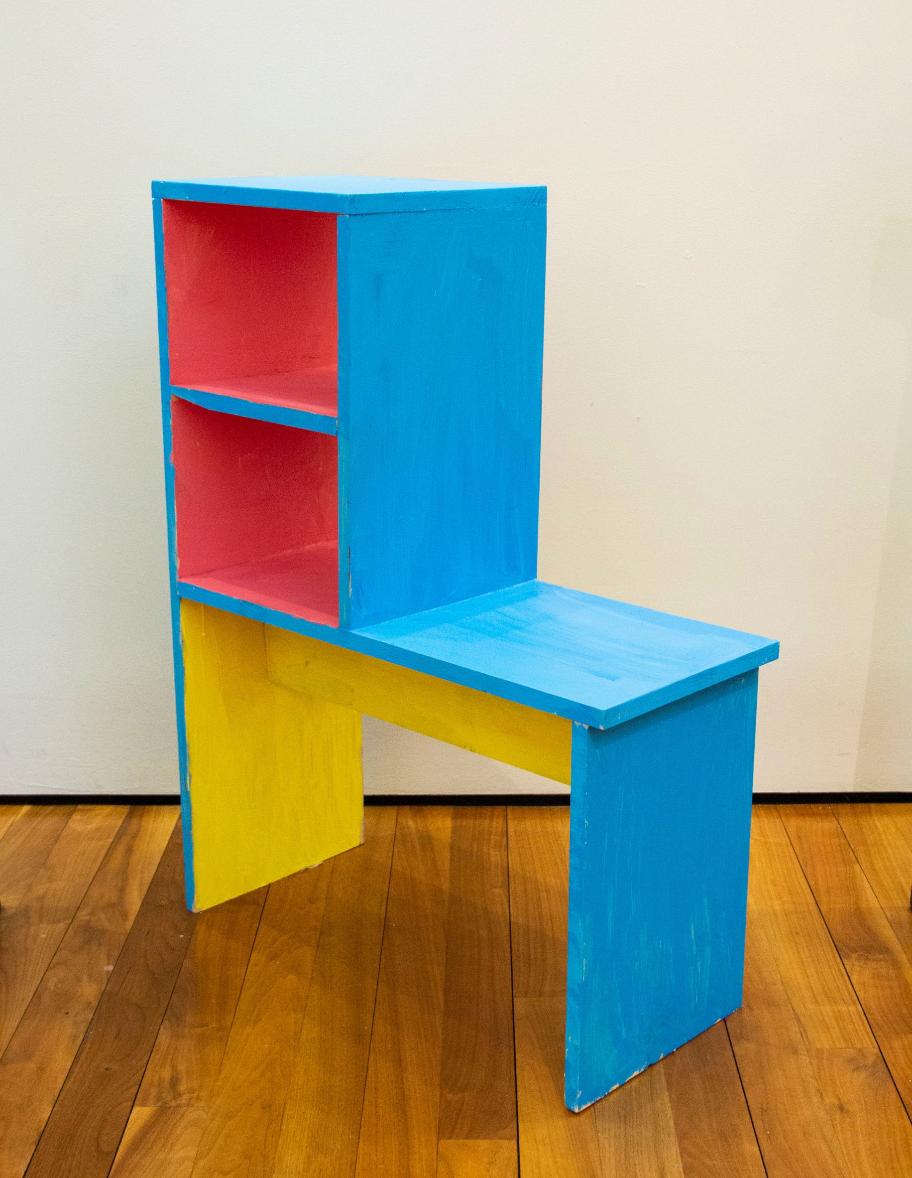 Chair with shelves built into the backrest, painted in flat planes of blue, pink and yellow