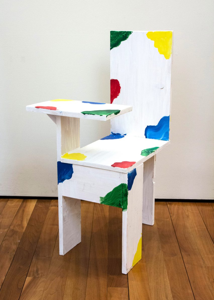 Simple chair with attached desk, painted white with splotches of bold blue, yellow, red and green colour