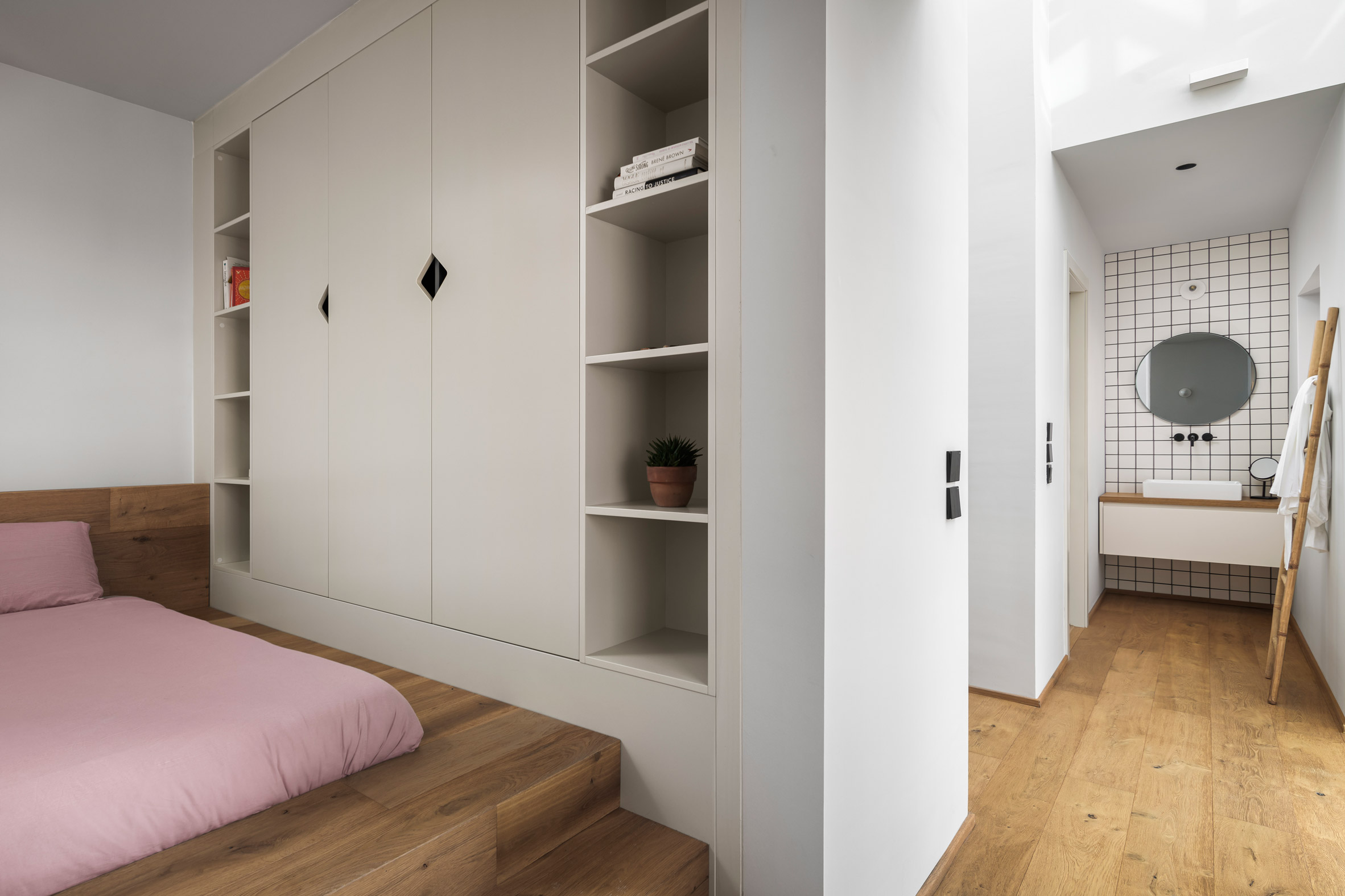 Bedroom inside La Serenissima house by Valentino Architects with raised wooden bed and small white-tiled bathroom area