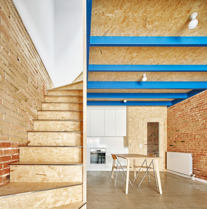 An oriented strand board staircase rises against an exposed brick wall at 105JON