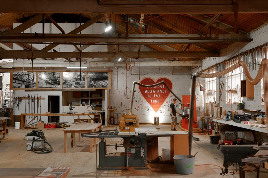 Interior of the Zero Waste Repurposing hub with work benches in the foreground and a heart-shaped mural in the back reading 'pledge allegiance to the land'