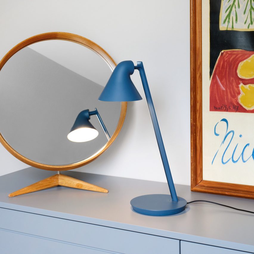 The Louis Poulsen NJP Mini LED Table Lamp in petrol blue standing in front of a mirror and framed poster