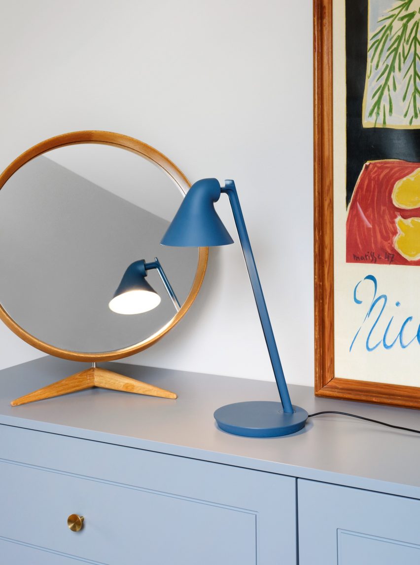 The Louis Poulsen NJP Mini LED Table Lamp in petrol blue standing in front of a mirror and framed poster