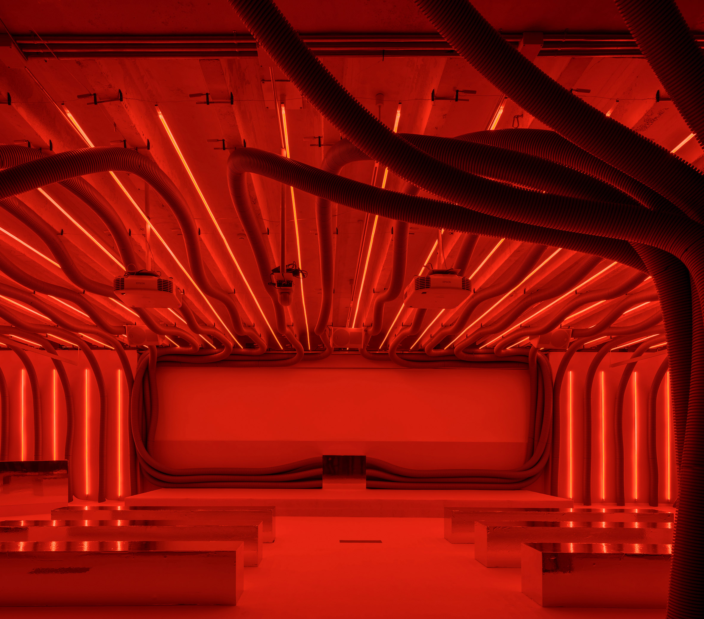 Lecture hall filled with corrugated plastic tubes and red neon light in installation by Pareid