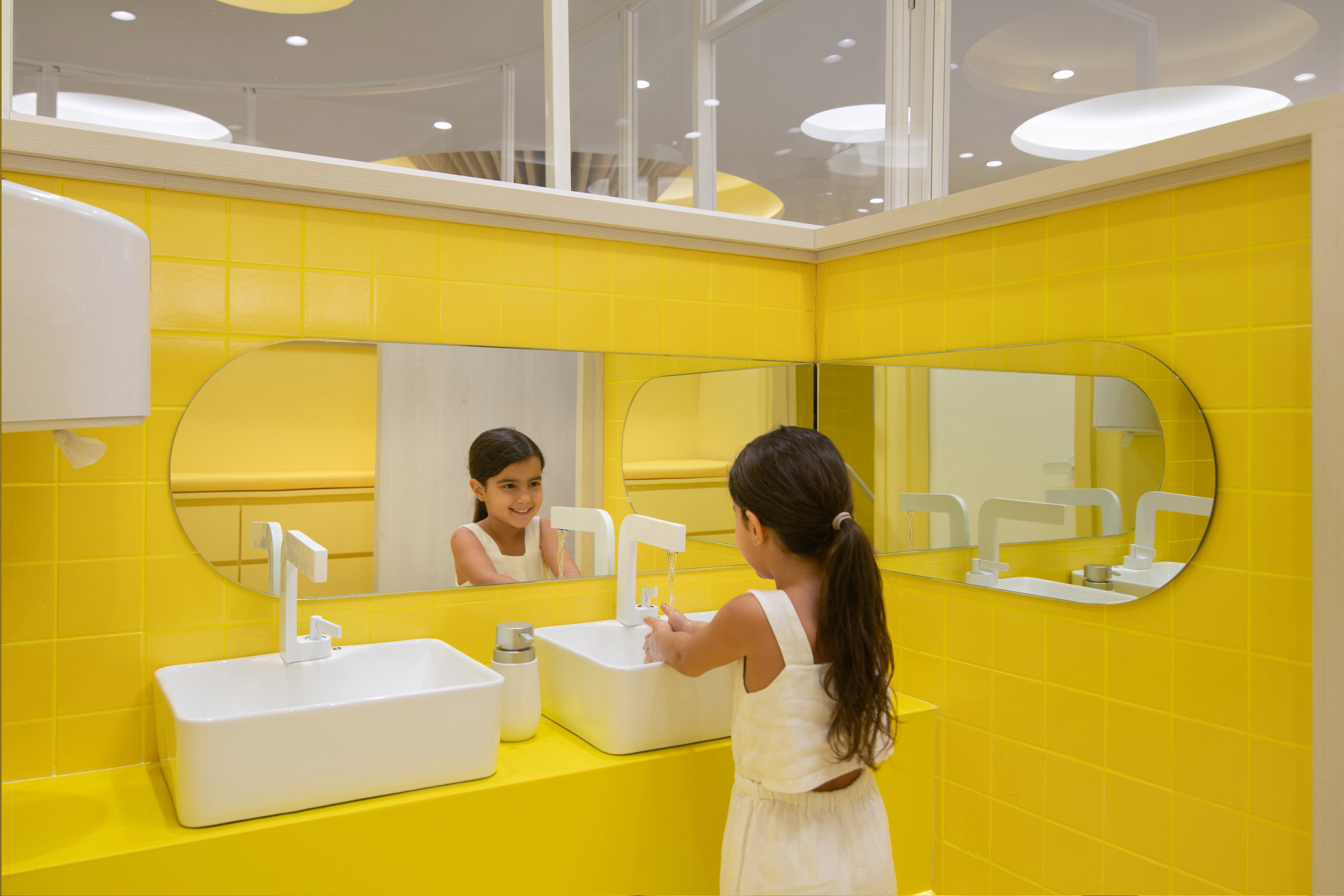 A girl washing her hands in a yellow bathroom