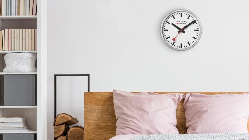 A Mondaine SBB Station Wall Clock hangs in a minimal bedroom