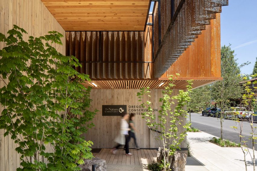 Entryway into a building with foliage, wood panels and weathered metal cladding