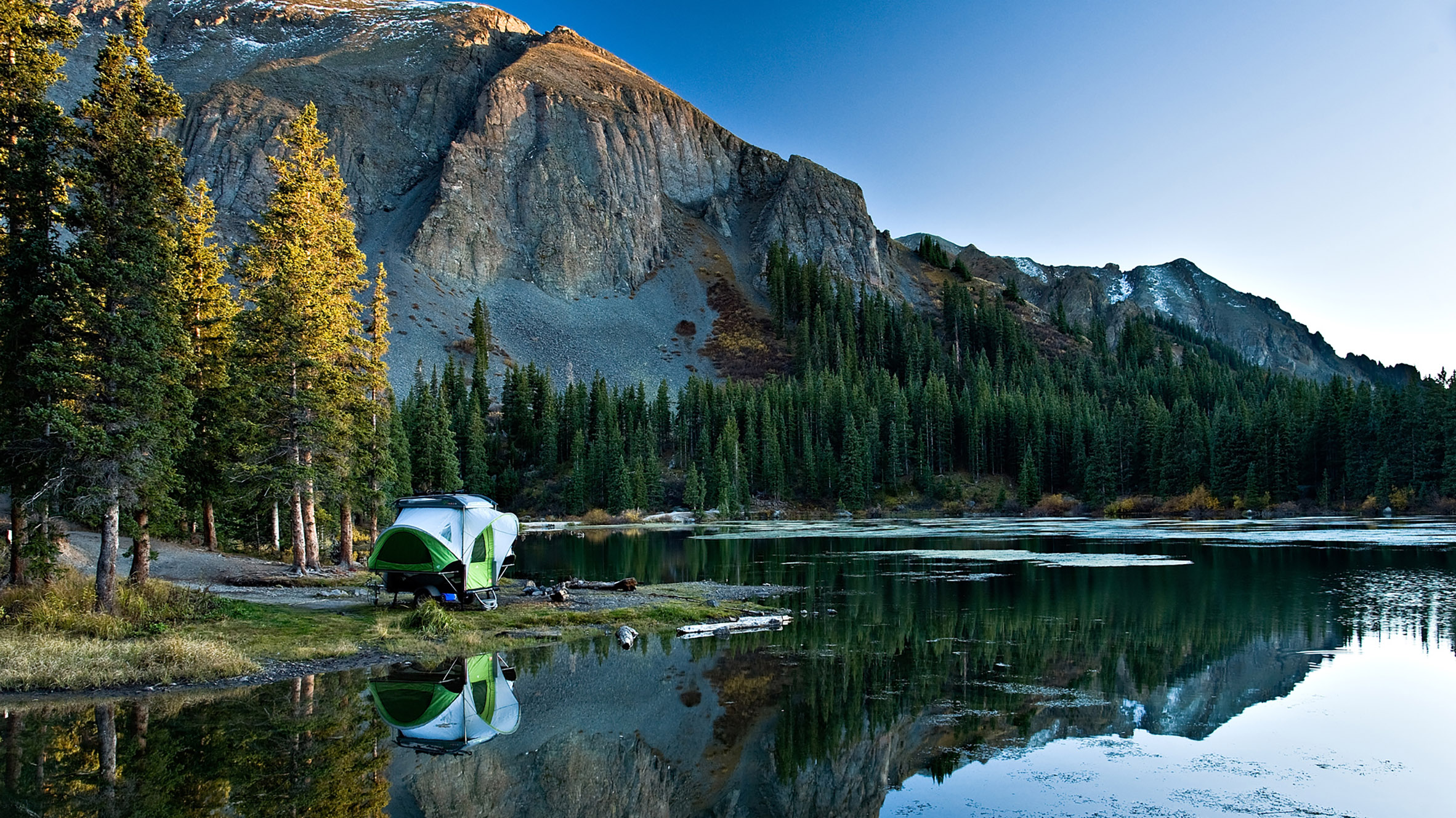 SylvanSport Go camping trailer parked by an isolated lake surrounded by mountains