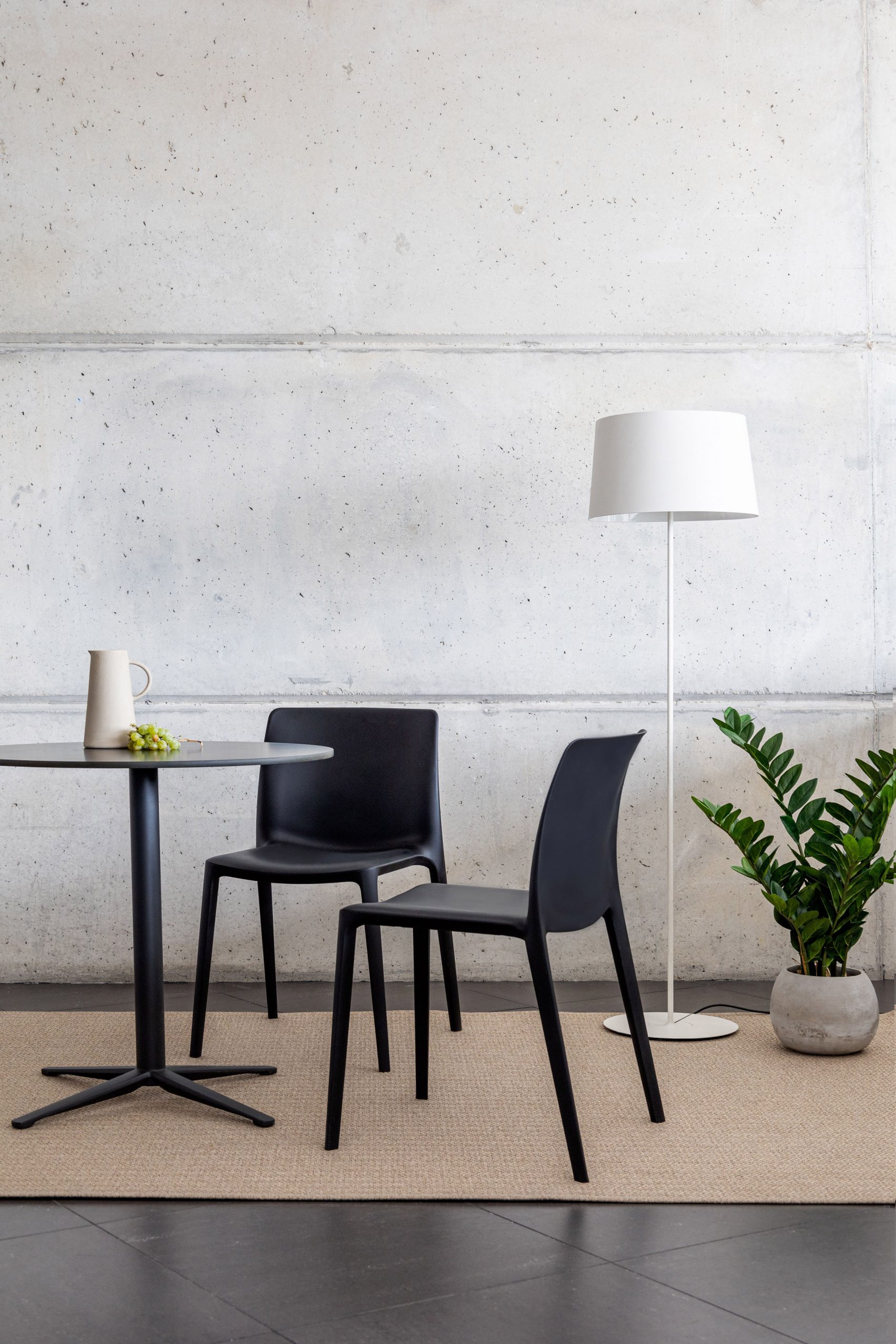 Two black Fluit chairs by Actiu next to a table, plant and lamp