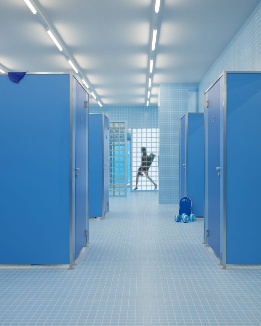 Темно-синие кабинки для переодевания заполняют раздевалки, имитирующие бассейн.