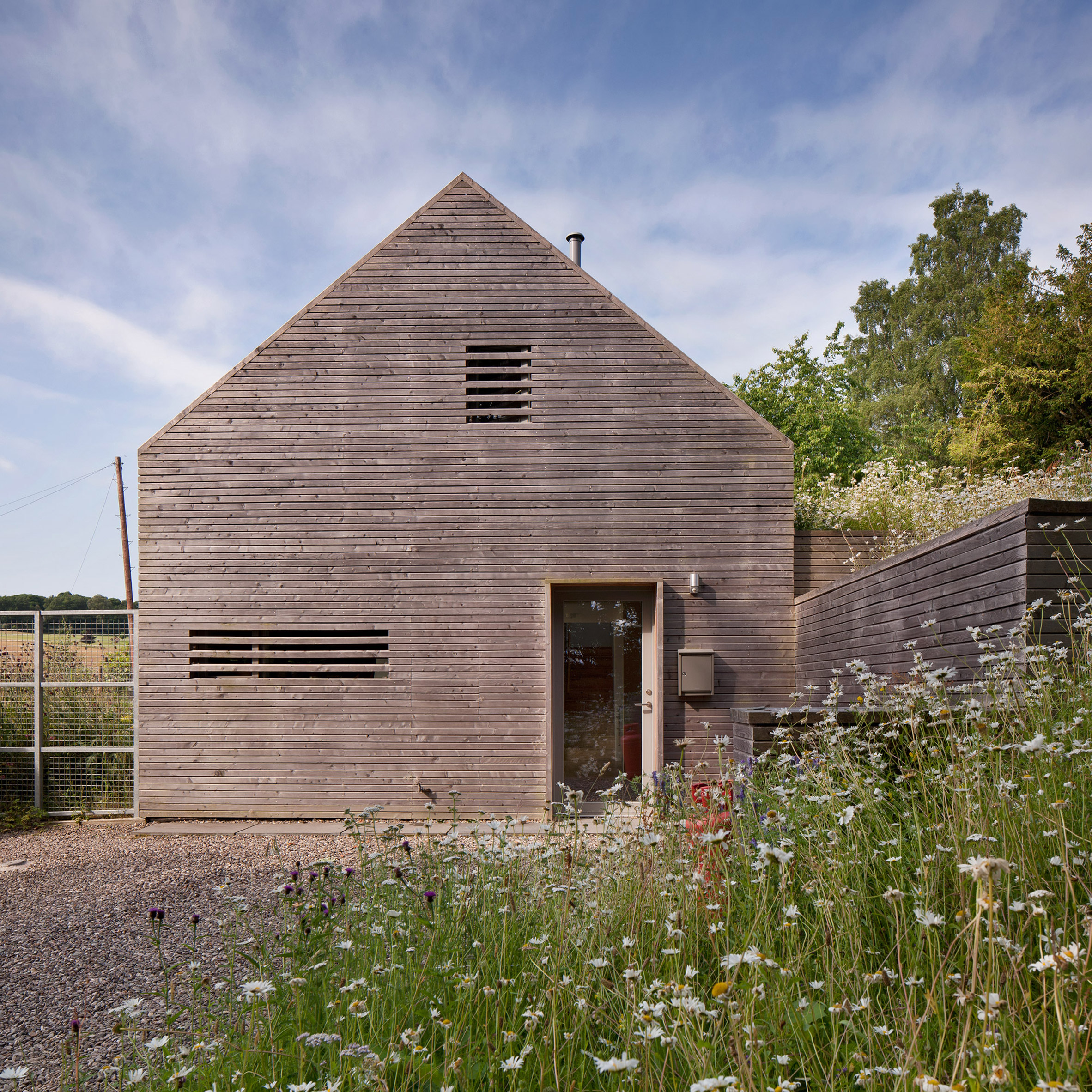 La parte delantera de la estructura de granero cubierta de madera de Mary Arnold Forster Architects en un área cubierta de hierba