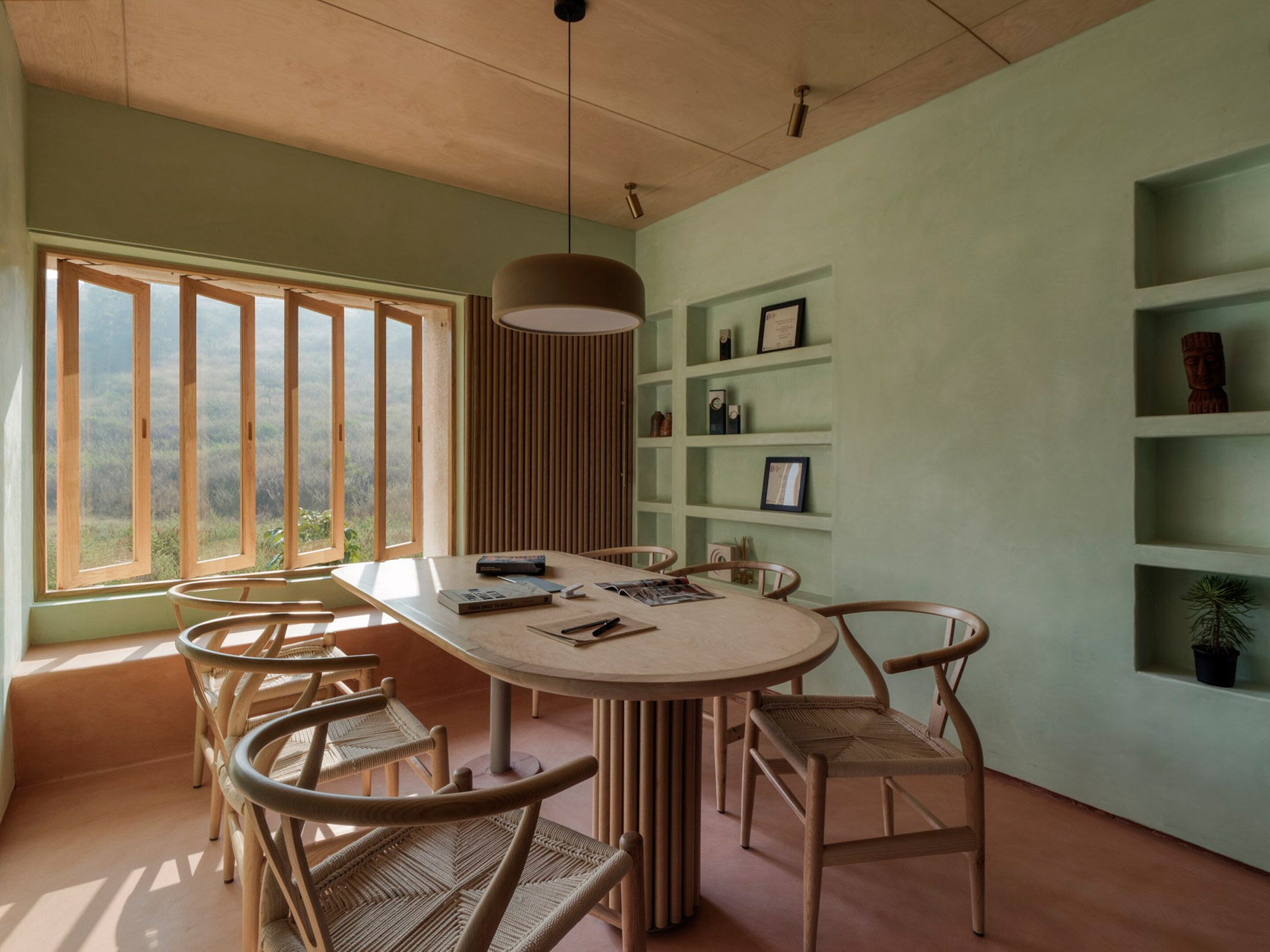 Sala de reuniones con paredes de color verde claro y muebles de madera en un estudio en Pune, India