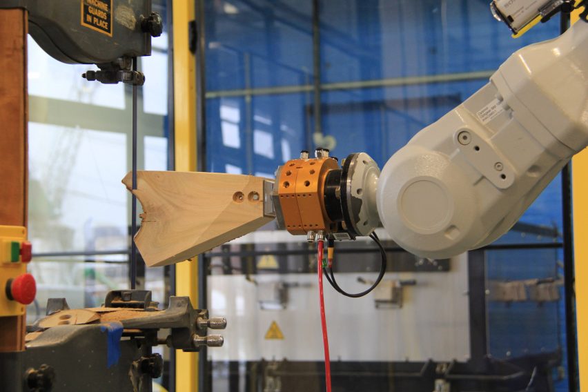 Robot arm pushes piece of wood into a band saw