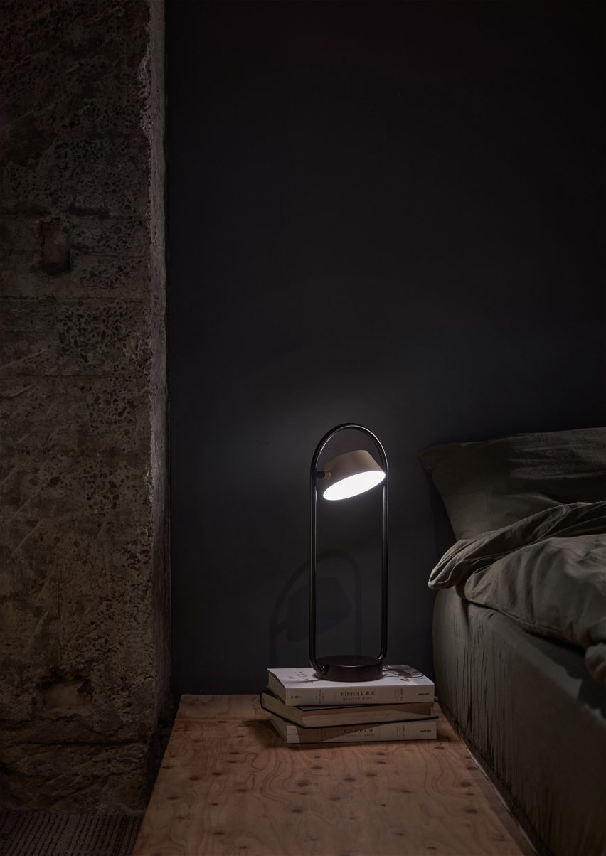OLO table lamp in a dark painted bedroom placed on top a stack of books next to the bed
