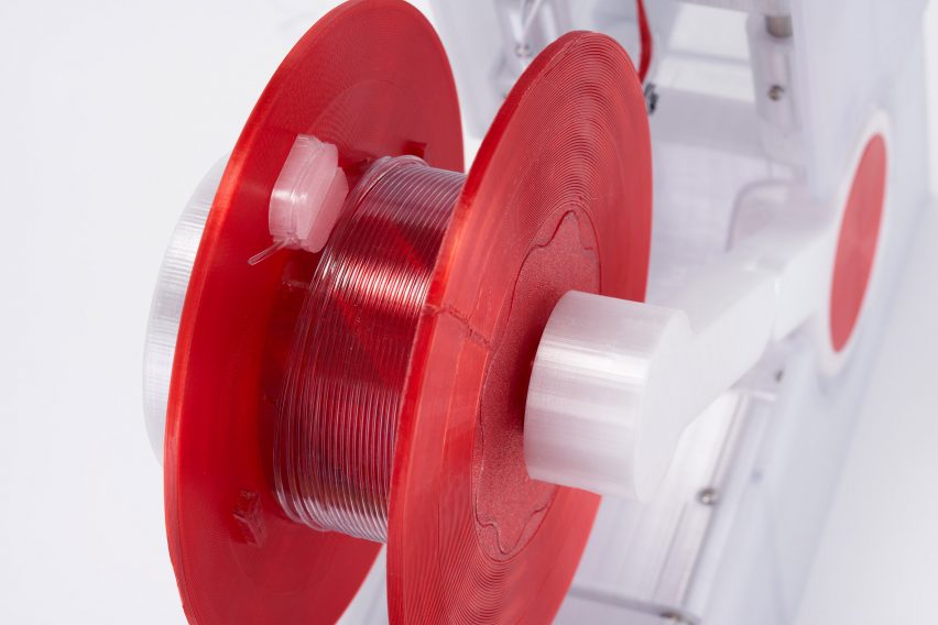 Recycled plastic filament on a red spool in recycling machine by Reiten Cheng