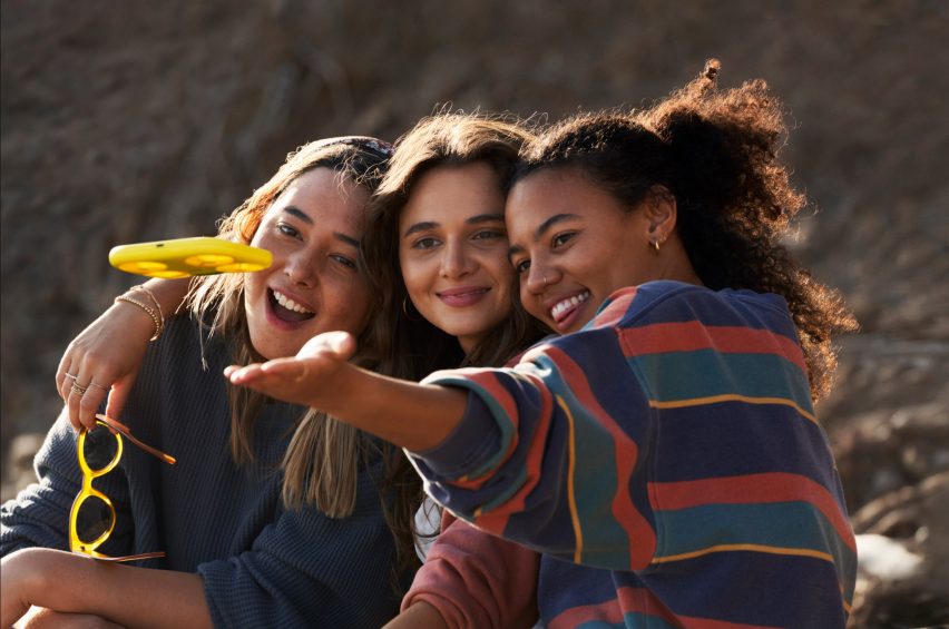 Three young women pose for a photo in front of a hovering yellow drone