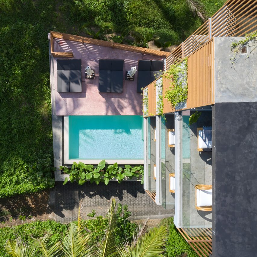 Aerial view looking down a hotel facade towards a pool with a pink deck