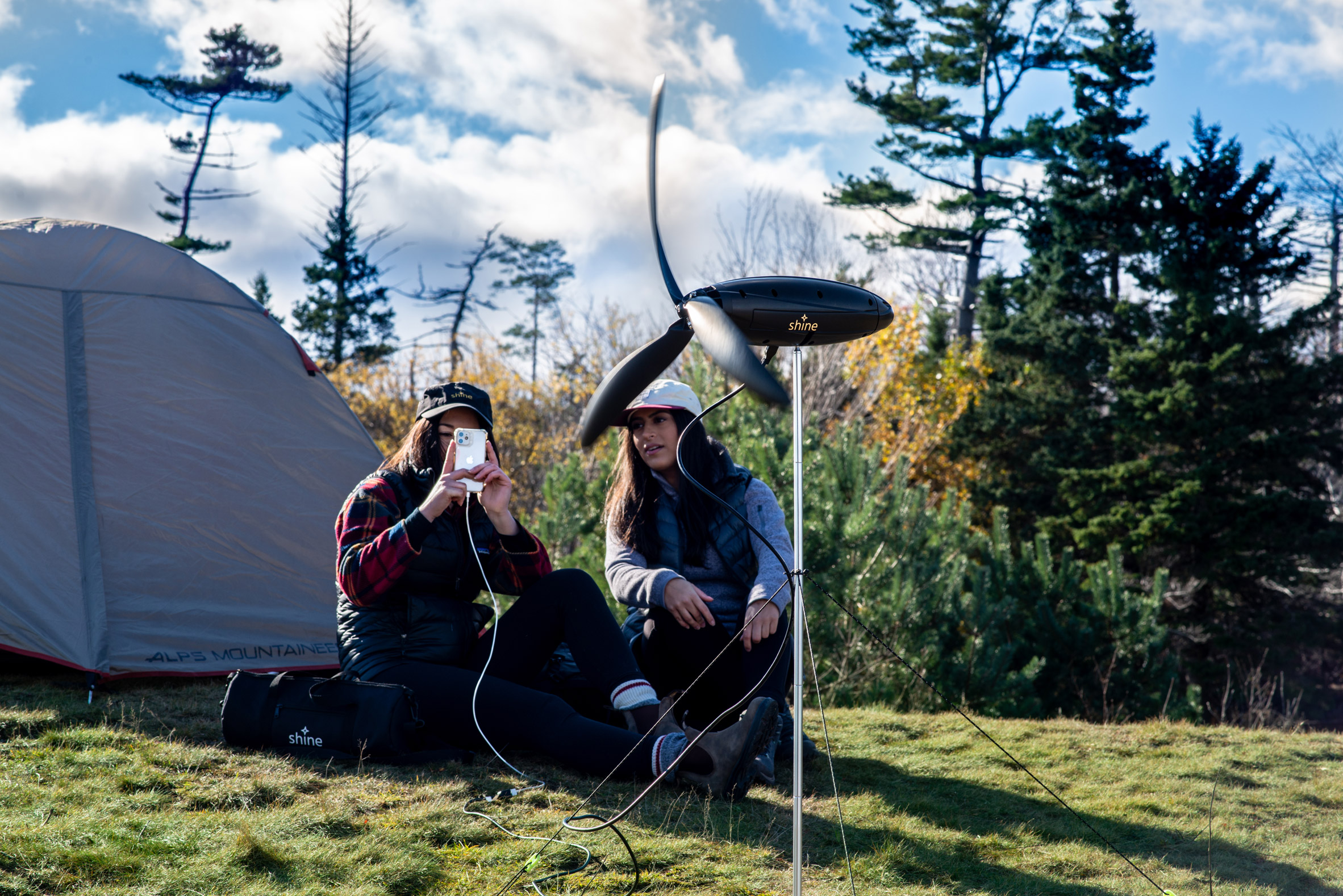 Wind turbine set up in front of two people sitting in front of their tent in the wilderness