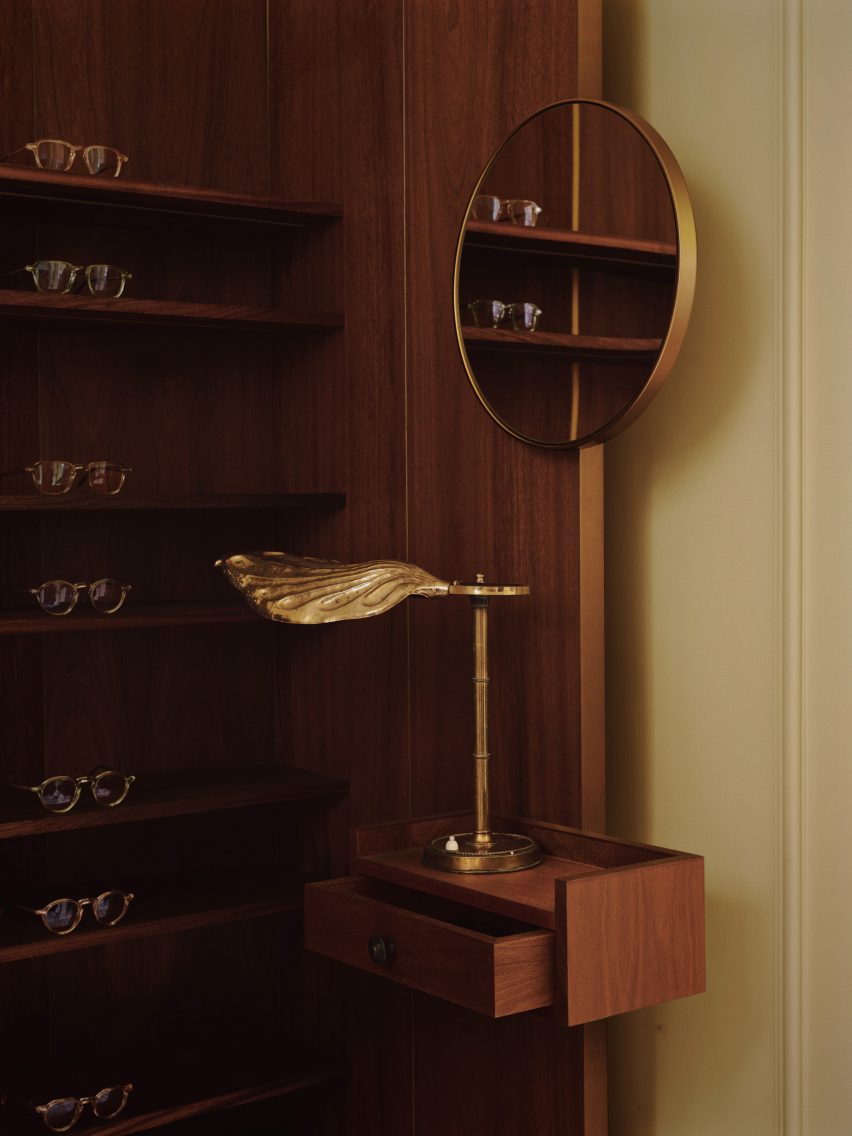 Close up of wooden display stand and leaf-shaped brass lamp in eyewear shop by Child Studio