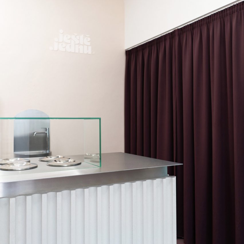 Steel and concrete serving counter next to the deep eggplant-colored curtain in the Ješte Jednu ice cream shop in Brno by Holky Rády Architektur