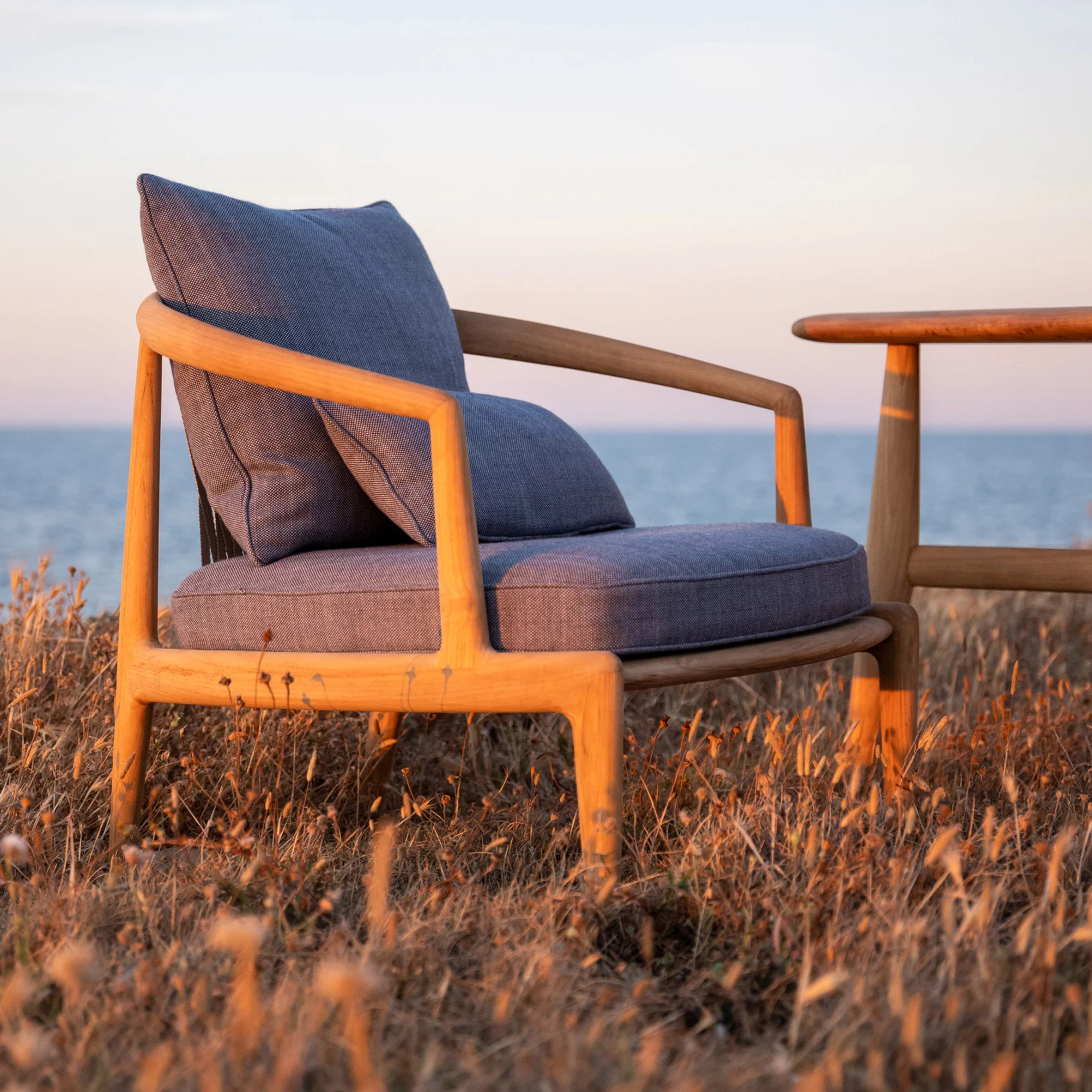 The Poltrona Frau Secret Garden armchair on a grassy patch with a setting sun sky