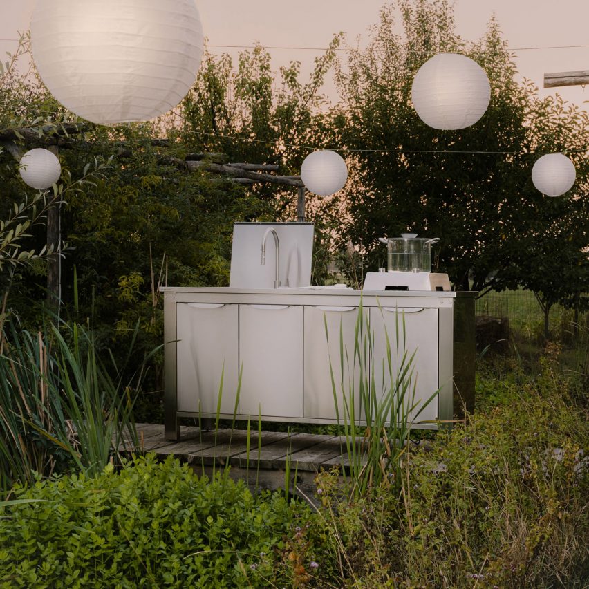 Metal finish kitchen on garden deck at sunset with spherical paper lampshades above