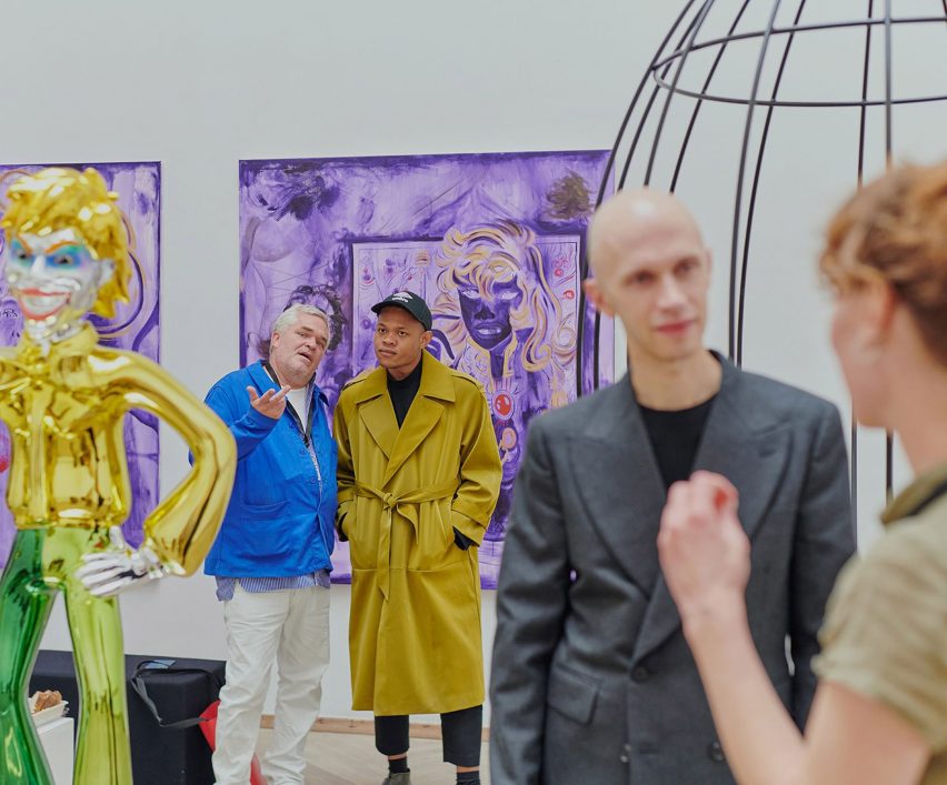 People looking at a gold sculpture, a wired sculpture and a purple painting