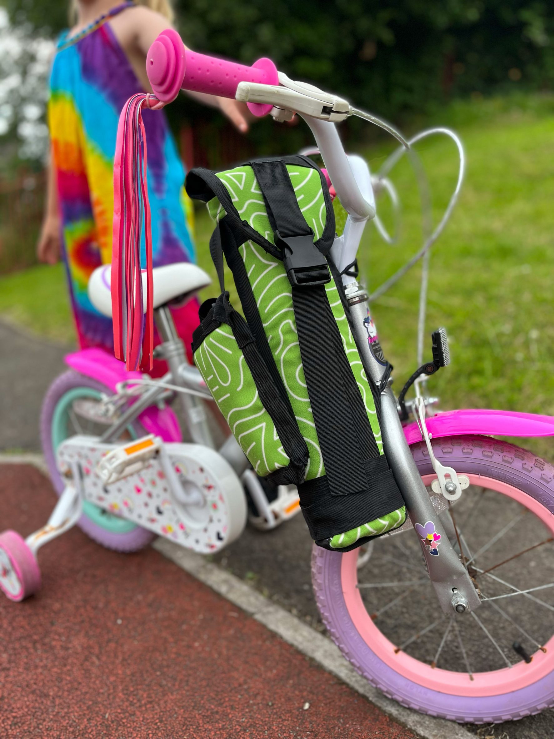 Photograph showing green and black strapped carry case attached to pink children's bike