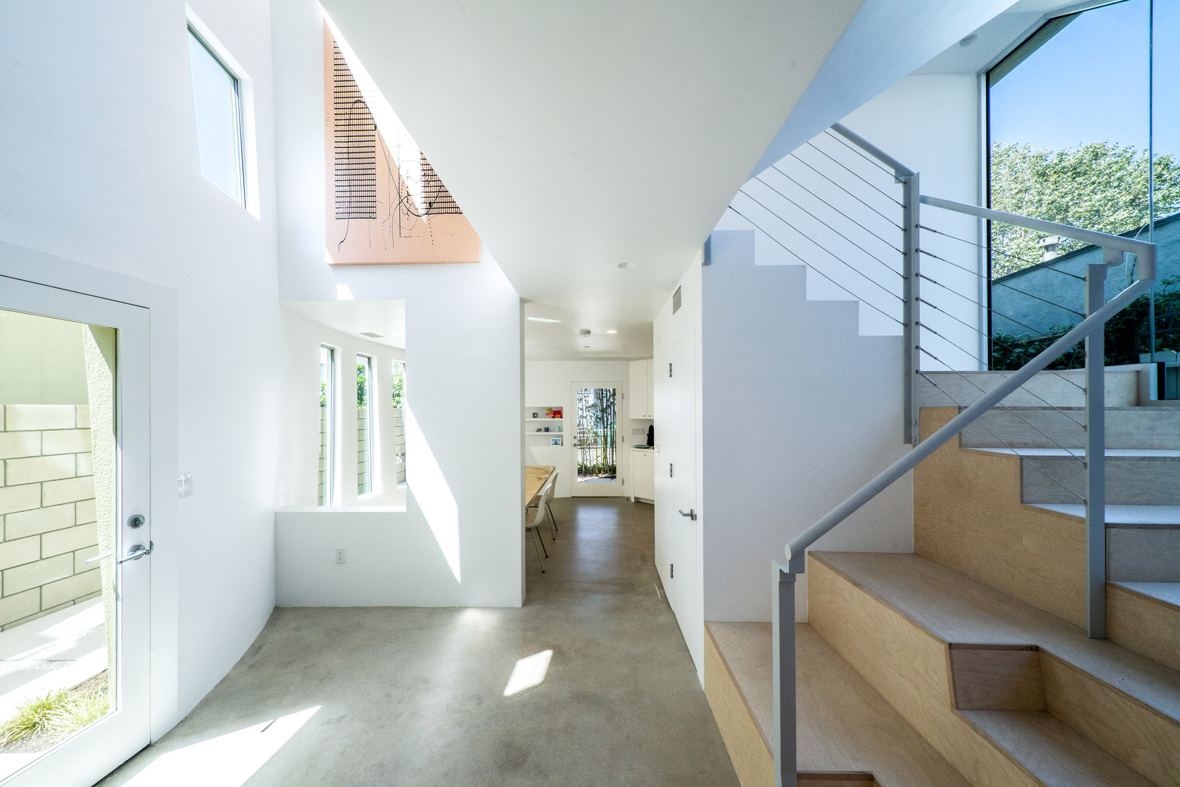 Light entryway of Los Angeles home with plywood staircase and white walls