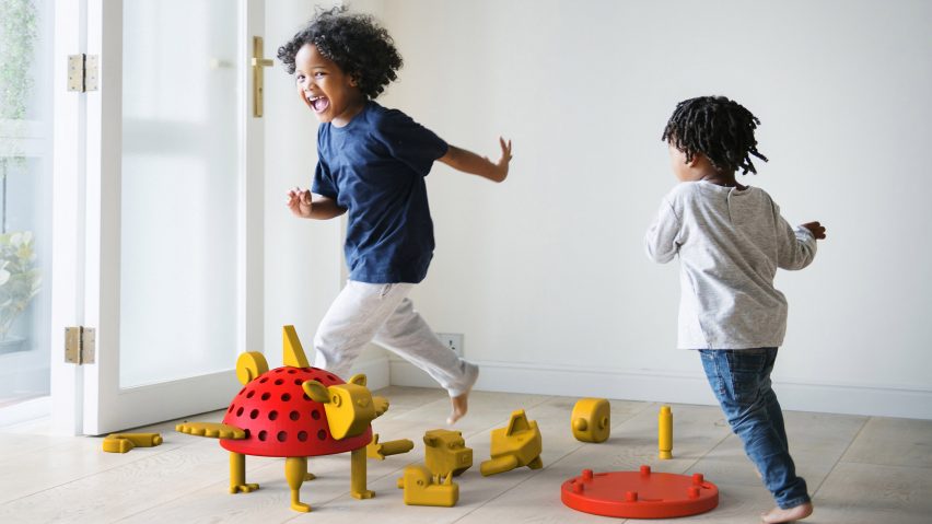 Two children playing around a red and yellow constructible toy