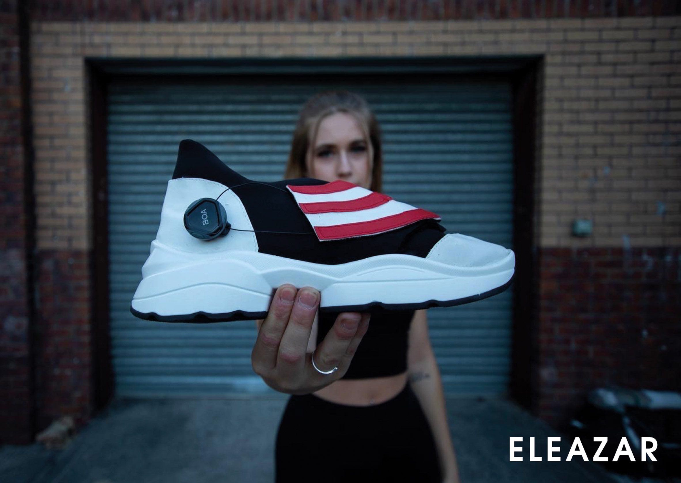 Photograph showing figure in front of urban garage holding black and white trainer shoe