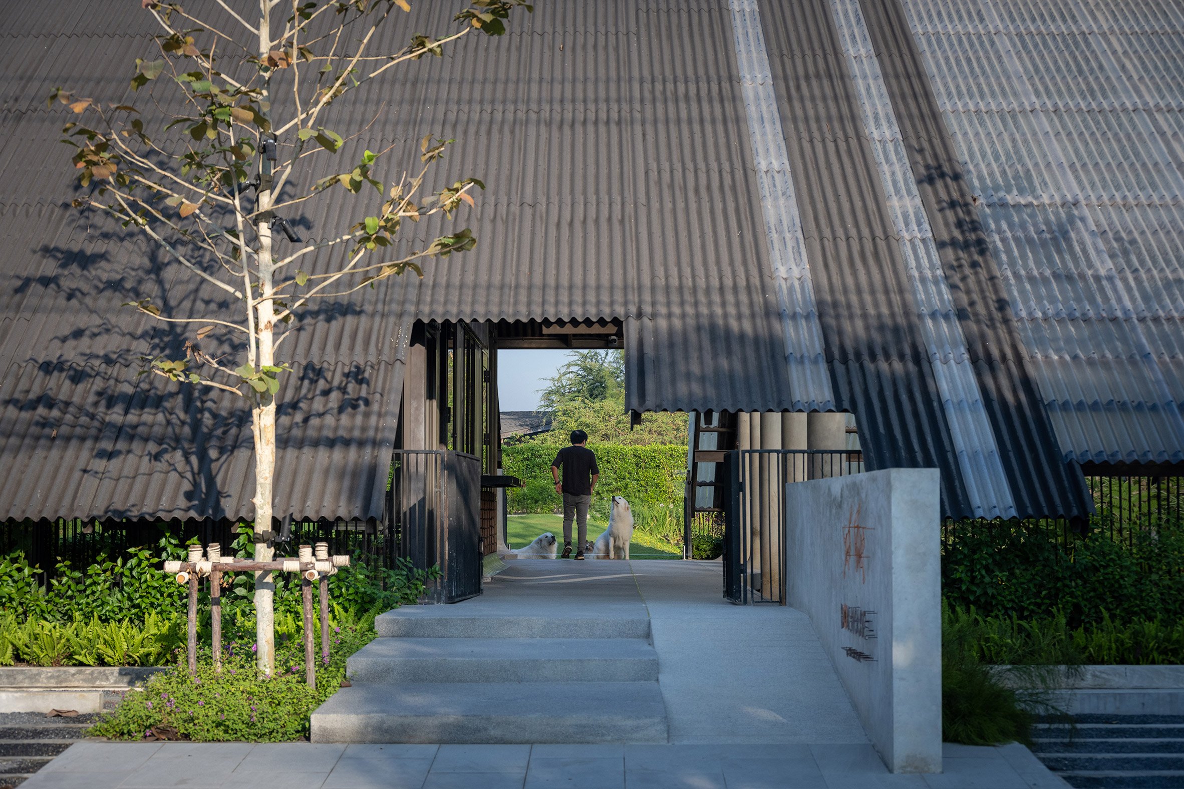 Concrete steps lead to building with corrugated roof by EKAR Architects