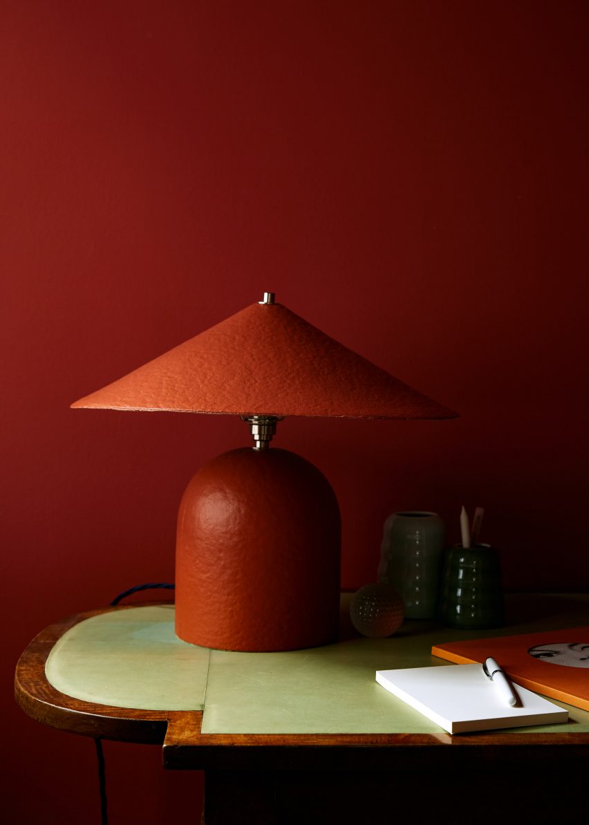 Curved red lamp made of paper pulp in front of wall