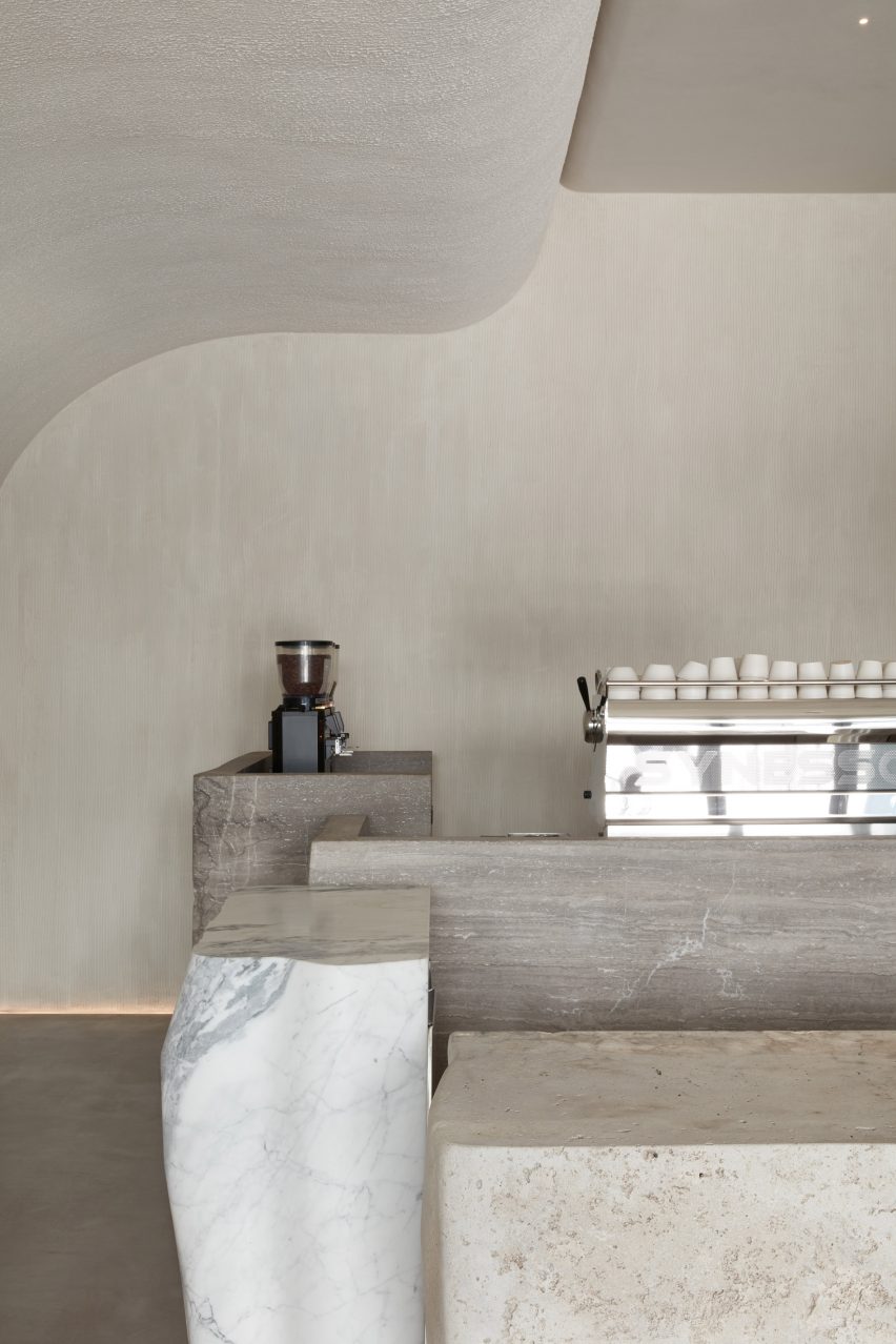 Plastered walls and a curved ceiling surrounding organically shaped marble units in Orijins coffee shop