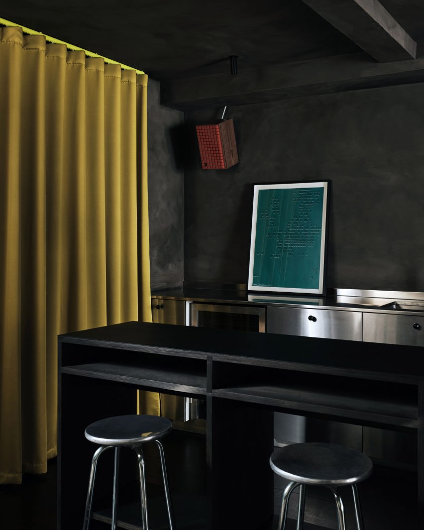 Black table and stools in office basement with dark walls and yellow curtain