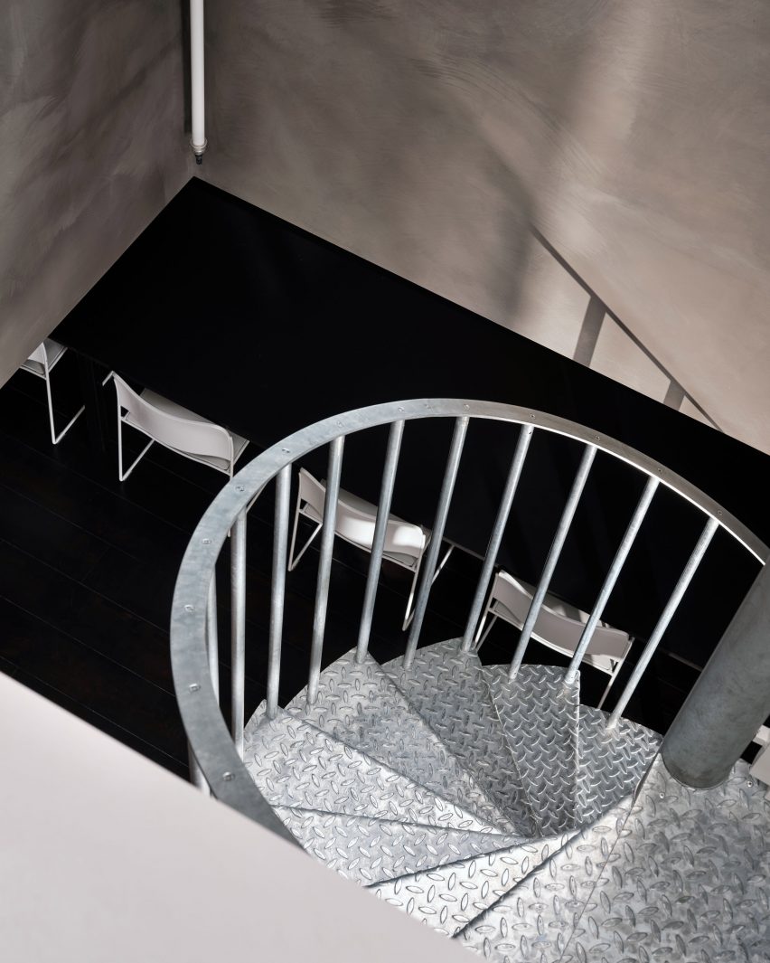 Metal spiral staircase leading to basement in office by Cake Architecture