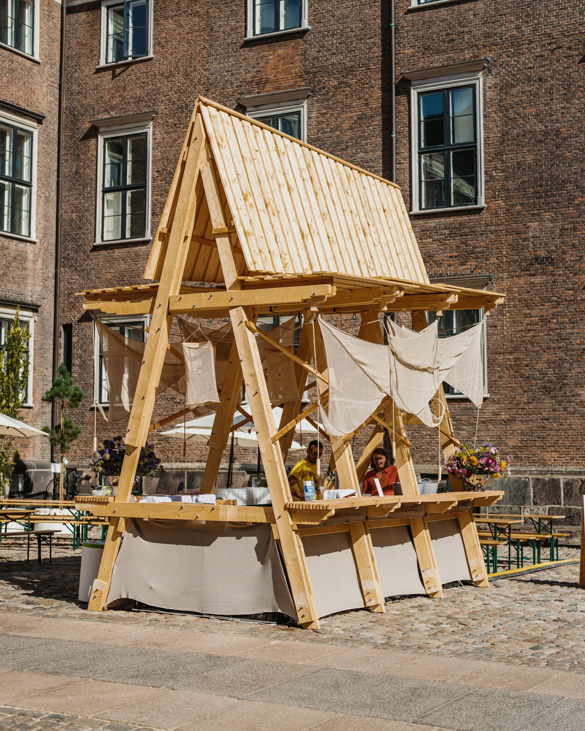 Timber A-frame pavilion with hemp wings in courtyard