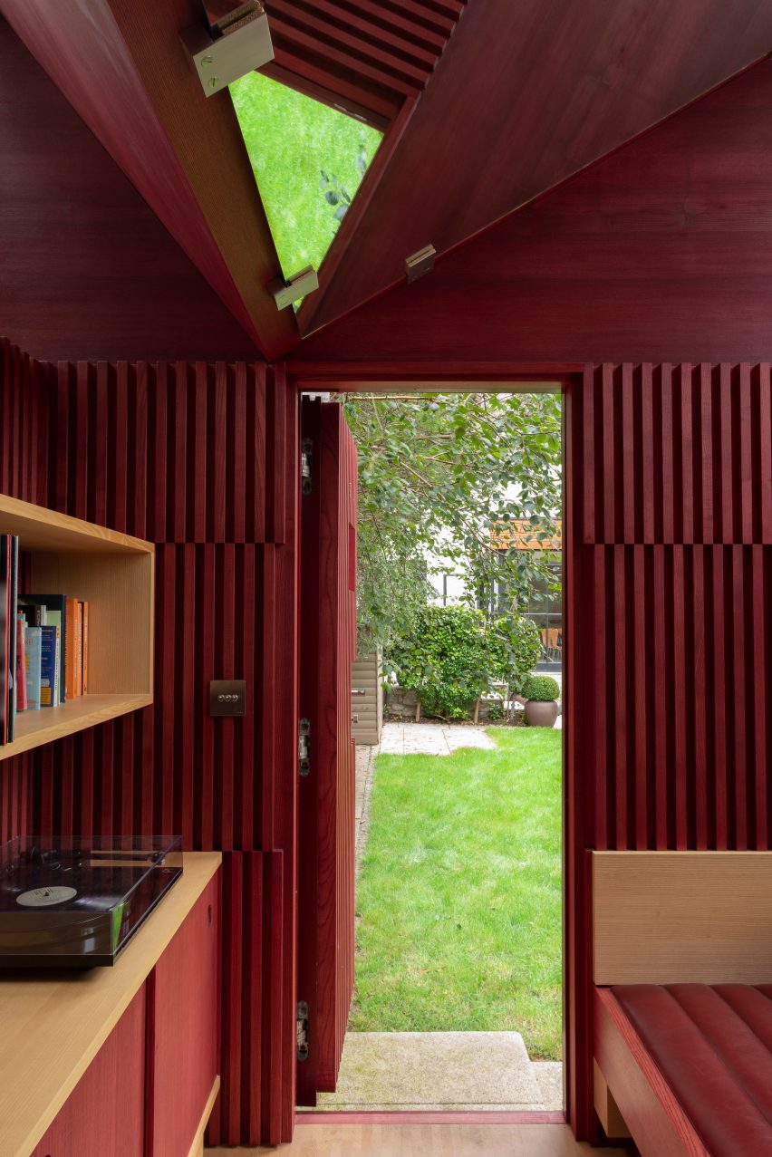 Red-stained timber battens arranged on walls of writer's hut in Ireland with view to garden