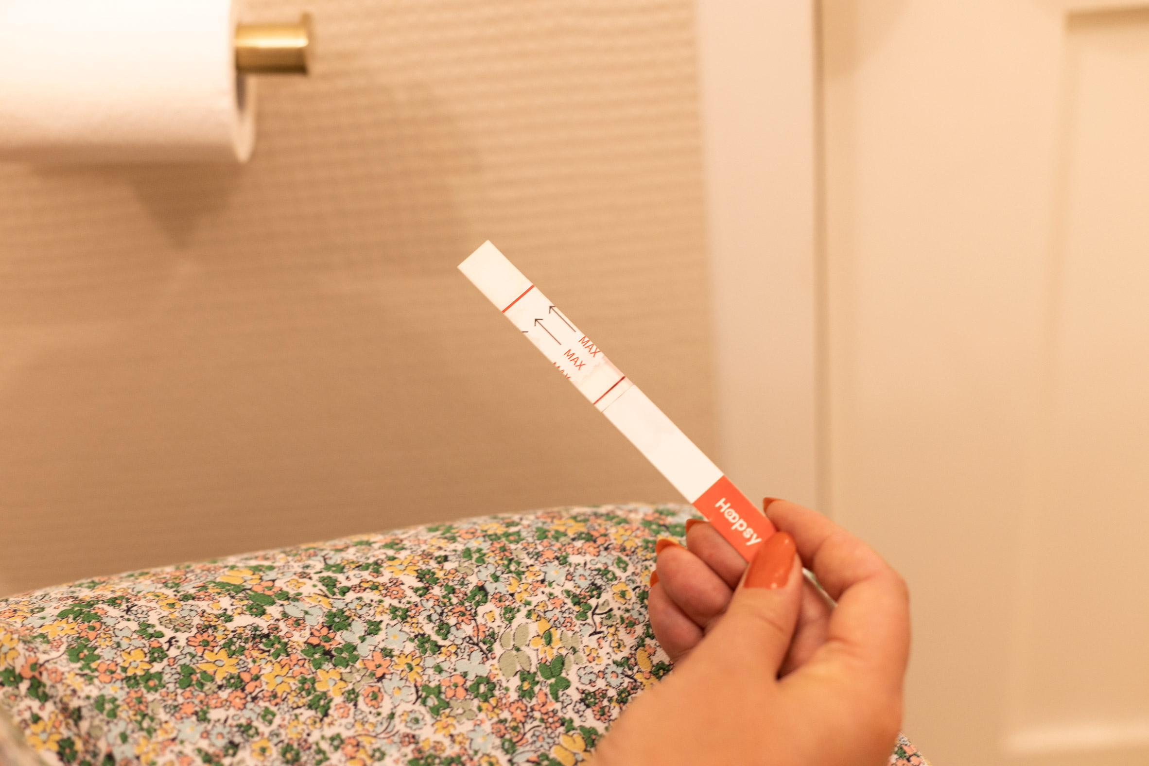 Woman's hand holds a Hoopsy test strip while sitting in a bathroom